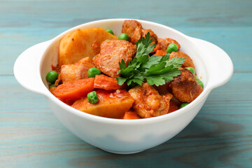 Delicious cooked stew in bowl on light blue wooden table, closeup