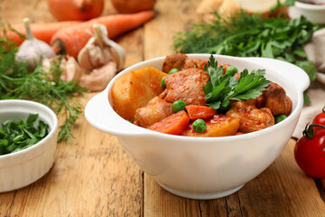 Delicious cooked stew in bowl and ingredients on wooden table, closeup