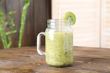 Tasty smoothie in mason jar and cut kiwi on wooden table, closeup
