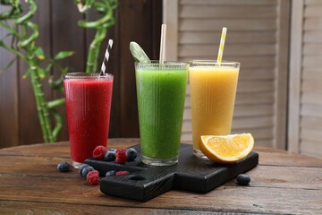 Different tasty smoothies in glasses and ingredients on wooden table, closeup