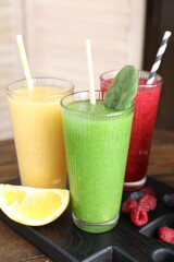 Different tasty smoothies in glasses and ingredients on wooden table, closeup