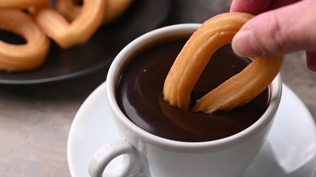 Hand dipping a churro in a cup of hot chocolate