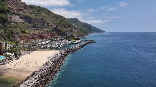 Aerial over Calheta breakwater and beach toward marina along Madeira coastline