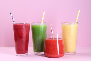 Different tasty smoothies in glasses on pink background