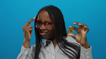 Woman holding bitcoin with confident gesture against isolated blue background, showcasing modern finance and cryptocurrency trends.
