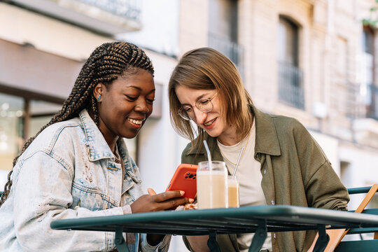 Multiethnic women enjoying coffee outdoors watching content on smartphone together