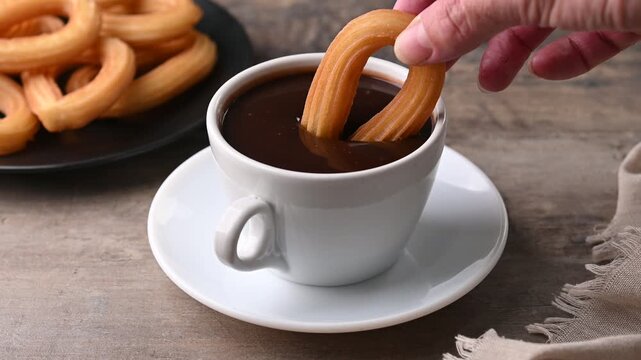 Hand dipping a churro in a cup of hot chocolate
