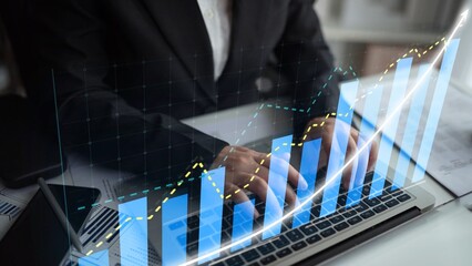 A business professional conducts a detailed analysis of financial trends using a laptop, data charts, and graphs in a contemporary office environment. Copula