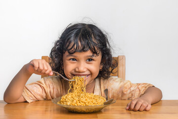 A happy little Asian girl eating fried noodles. A plate of fried noodles.