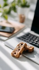 Healthy granola bars with chocolate chips on laptop at bright workspace, cozy morning coffee break, remote work lifestyle concept