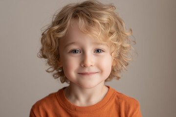 Naklejka premium a cute 4-year-old boy with light blonde hair, wearing an orange t-shirt, soft smile, natural lighting, light gray studio background