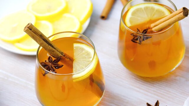 Two glasses warm spiced cider with cinnamon sticks, star anise, and lemon slices.