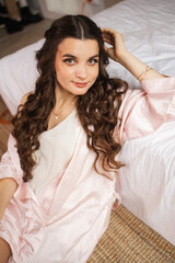 A beautiful bride poses gracefully by a sunlit window, wearing a delicate lace robe. The light highlights her serene expression and the intricate details of her bridal attire