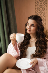 The bride is going to the wedding, drinking coffee sitting at the window. bride in a silk robe, morning of the bride, wedding day.