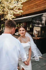 Naklejka premium Wedding photography, portrait of happy smiling newlyweds, stylish groom and beautiful young brunette bride, walking and holding hands, outdoors on the street in the city.