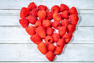 Heart shape made of fresh raspberries on white wooden background. Concept of love, health, vegan food, and organic lifestyle. 