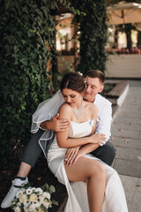 Fototapeta premium Wedding photography, portrait of happy smiling newlyweds, loving couple, fashionable groom and beautiful cute brunette bride, hugging outdoors on the street in the city, in the park.