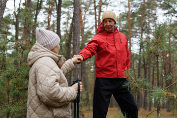 Two hikers share a moment in the forest, holding hands and smiling as they explore the natural surroundings on a bright day