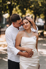 Obraz premium Wedding photography, portrait of happy smiling newlyweds, fashionable groom and beautiful cute brunette bride, hugging outdoors on the street in the city, in the park.