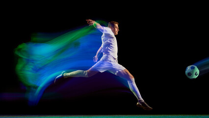 Soccer player kicking ball with green and blue neon motion trail on dark field. Concept of...
