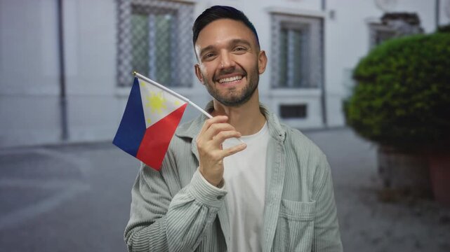 Young man smiling holding philippine flag outdoors in urban street setting showcasing national pride and cultural identity in city environment.