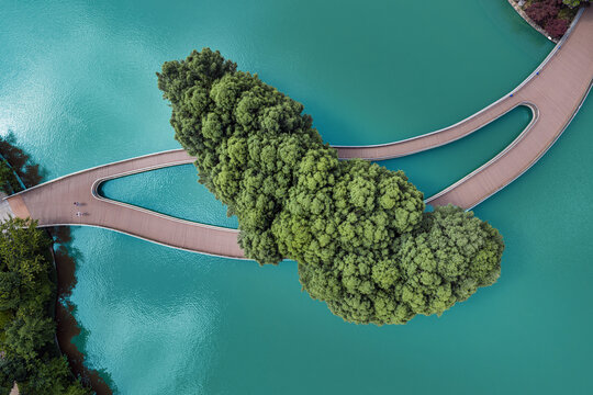 Aerial view of a jade-colored lake embracing a verdant island, bisected by a gracefully curving bridge, Panglong Waterfall Park, Kunming, China.