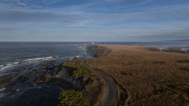 Aerial view of the Point Arena Lighthouse standing tall against the vast Pacific Ocean, the rugged coastline meeting the tranquil sea, Point Arena, California, United States.