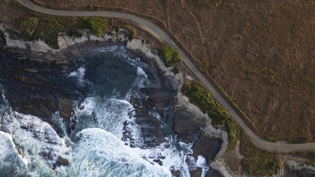 Aerial view of the rugged California coastline where the azure ocean meets the golden cliffs, a winding road tracing the edge, Mendocino, California, United States.