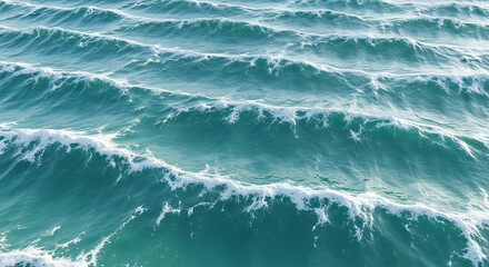 Aerial view of ocean waves rolling in parallel lines, creating a textured surface of blue water and white foam.
