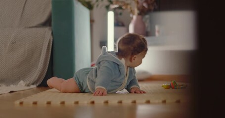 Baby lying on floor reaching forward with arms extended during tummy time, showing determination and effort in early crawling and motor skill development