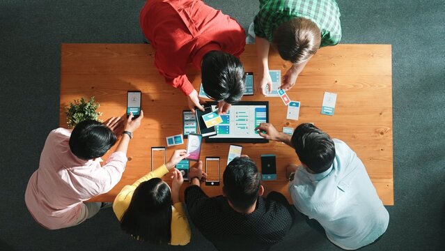 Top view of software developer team looking Ux Ui design for mobile phone interface from tablet while comparing and planning wireframe prototype designing together at creative workplace. Convocation.