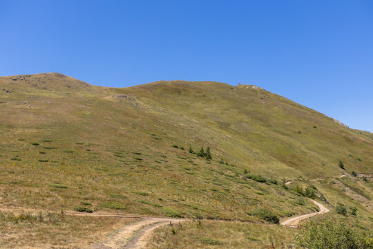 Winding dirt path on grassy hillside with clear blue sky in mountain landscape