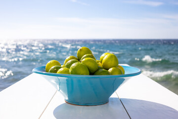 minimalist still life with vase of fresh limes on clean white table on seascape backdrop. fresh fruit background. coastal atmosphere