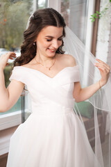Closeup shot of elegant, brunette bride in vintage white dress posing under veil closeup. Bride portrait wedding makeup and hairstyle, fashion bride. Beautiful bride in veil.