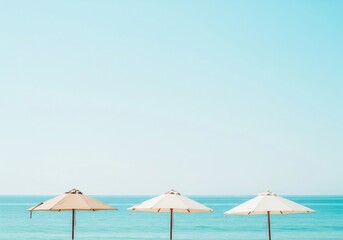 Fototapeta premium Minimal beach scene with three umbrellas against turquoise sea and clear blue sky, ample copy space