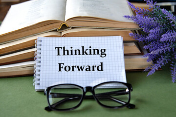 Notebook with THINKING FORWARD text on a green background with books and glasses