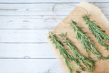 Bunches of fresh rosemary tied with twine, laid out on parchment over rustic white wood. Natural food preservation and autumn kitchen vibes