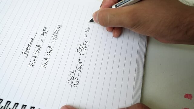 Person writing trigonometric formulas in a notebook with a pen