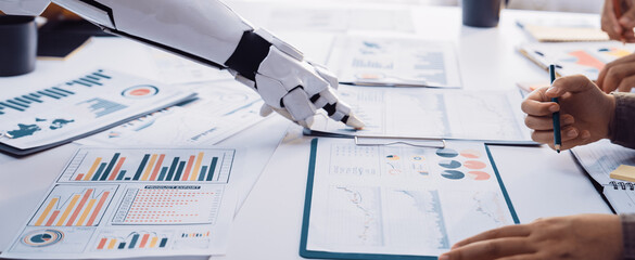 A robotic hand reaches for data papers during a corporate meeting, highlighting the synergy of...