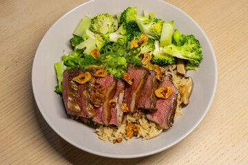 A plate of beef slices and broccoli over rice.