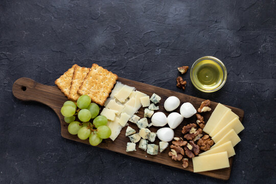 Gourmet cheese platter with crackers, grapes, walnuts, and honey on rustic dark background