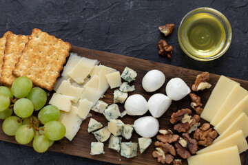 Gourmet cheese platter with crackers, grapes, walnuts, and honey on rustic dark background
