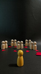A single yellow wooden figure stands apart from a group of wooden figures surrounded by scattered red hearts, symbolizing loneliness, exclusion, social disconnection, and emotional distance.