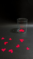 A single red heart is confined under a clear glass cup while other hearts lie freely around it, symbolizing emotional isolation, unrequited love and obstacles in relationships in a lonely atmosphere.