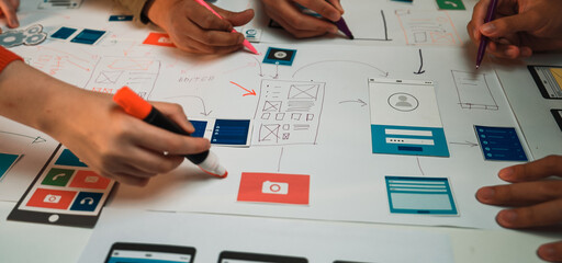 A group of creative individuals engaged in a productive design session for user interface layouts, utilizing colorful markers to annotate their sketches on a large paper. SACTR
