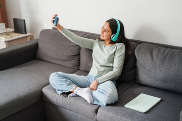 Female teen doing reel video for social media with smartphone while listening music with headphones...