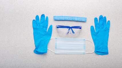 Medical face mask, glasses, hat and gloves laying on table flat lay view with copy-space