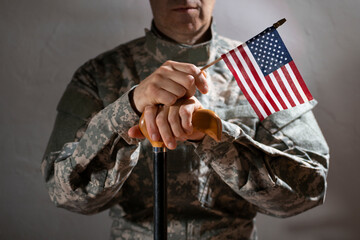 Soldier in camouflage uniform holding a cane and us flag symbolizing veteran support and resilience
