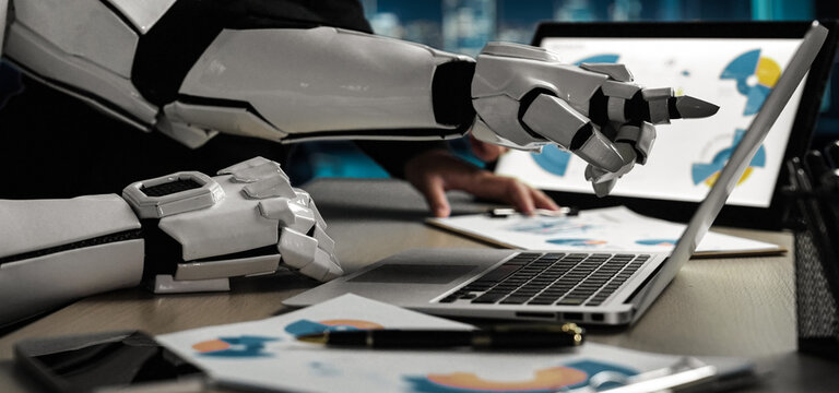 A futuristic robot hand interacts with a laptop in a modern office setting, analyzing data and charts, showcasing the fusion of AI technology with business.Noogenesis