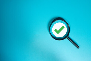 Quality Control (QC) and inspection concept. Magnifying glass focusing on a green checkmark, symbolizing approval, verification, and passing a quality audit on a blue background with copyspace.